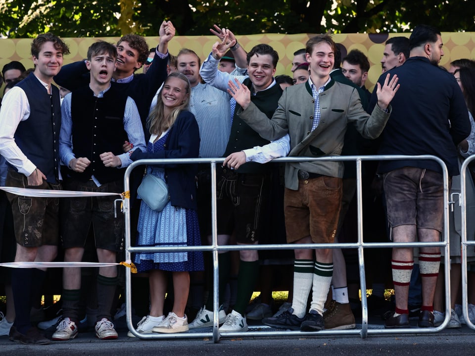 Gruppe von jungen Leuten in traditioneller Tracht hinter einem Zaun bei einer Veranstaltung.