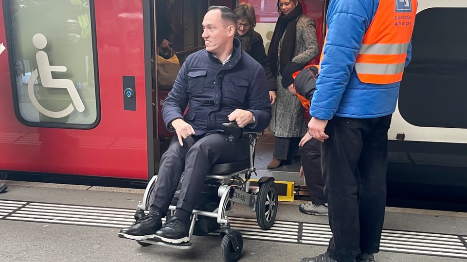 Islam Alijaj fährt mit seinem Rollstuhl aus dem Zug heraus, ein Angestellter der Bahnhofshilfe assistiert.