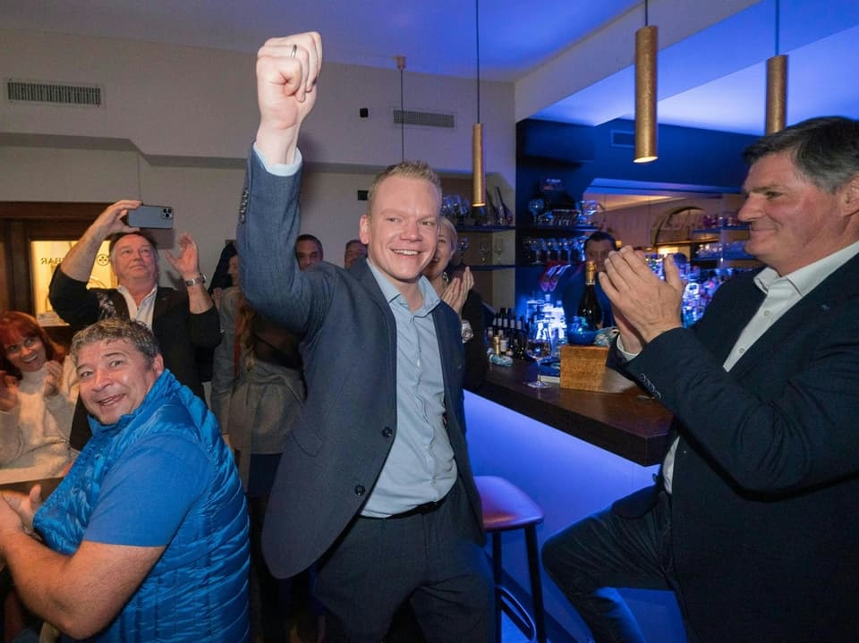 Gruppe von Menschen feiert in einer Bar, zentrale Person hebt den Arm.