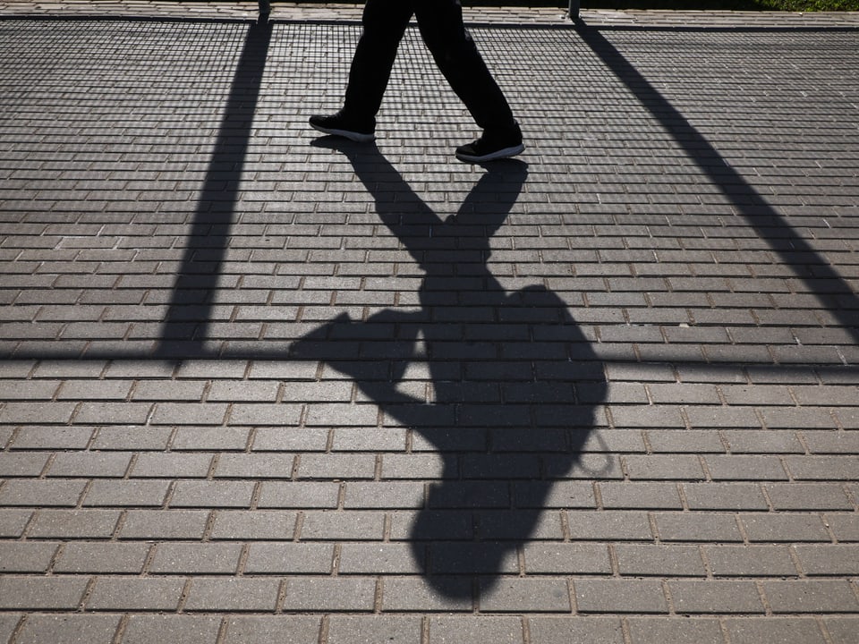 Schattensilhouette einer Person mit Rucksack auf Gehweg.