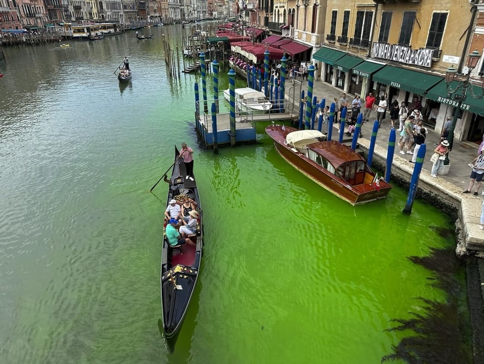 Blick auf den Canal Grande in Venedig. Eine Gondel fährt auf dem Wasser, das hellgrün leuchtet.