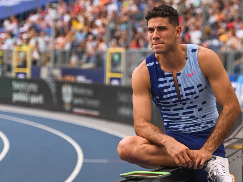 Ein männlicher Athlet in blauem Trikot sitzt am Rande einer Laufbahn.