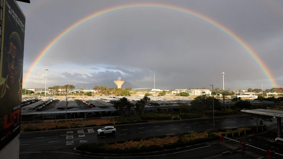 Regenbogen über Parkplatz bei bewölktem Himmel.