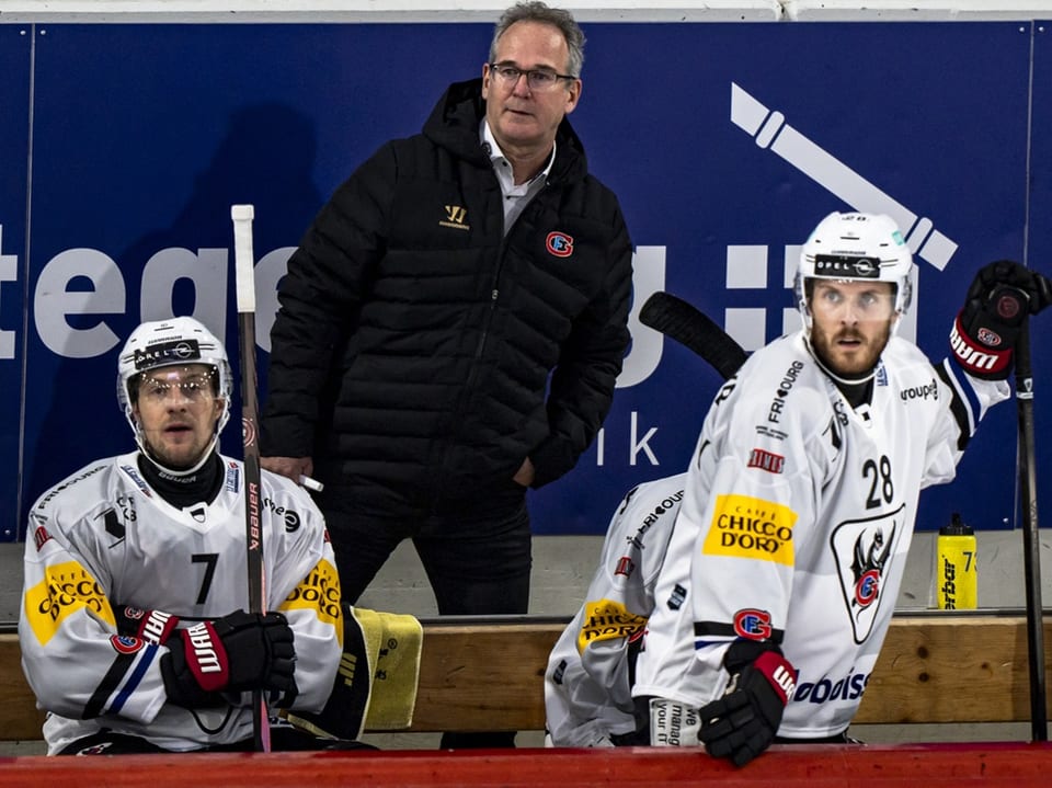 Eishockeytrainer steht hinter zwei Spielern auf der Bank.