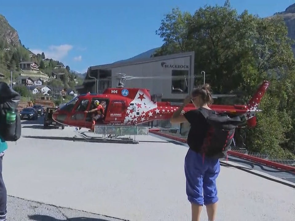 Person fotografiert einen Helikopter mit rot-weissem Sternenmuster vor dem Start auf einem Landeplatz.