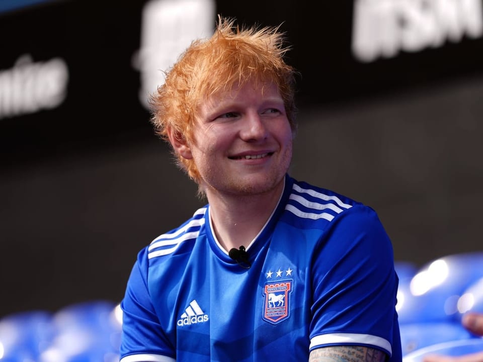 Mann in blauem Fussballtrikot lächelnd.