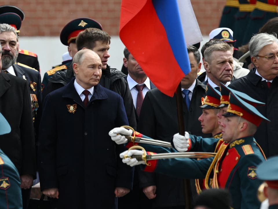 Militärparade mit hochrangigen Persönlichkeiten und russischer Flagge.