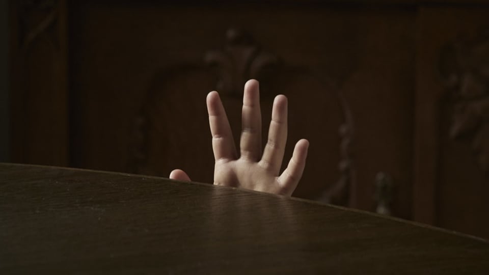 Eine kleine Hand kommt halb hinter einer schwarzen Tischplatte hervor. Symbolbild