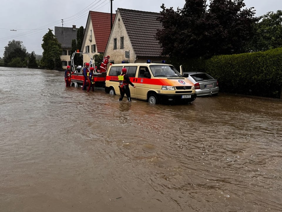Rettungsfahrzeug und Einsatzkräfte bei Hochwasser auf einer Strasse.