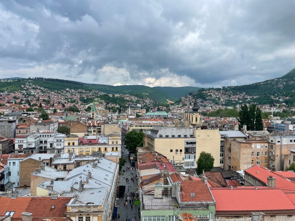 Panoramablick auf Stadt mit Wolken und Hügeln im Hintergrund.