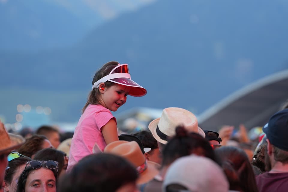 Kleines Mädchen mit Visier auf den Schultern eines Erwachsenen bei einem Festival am Open Air Lumnezia 2024.