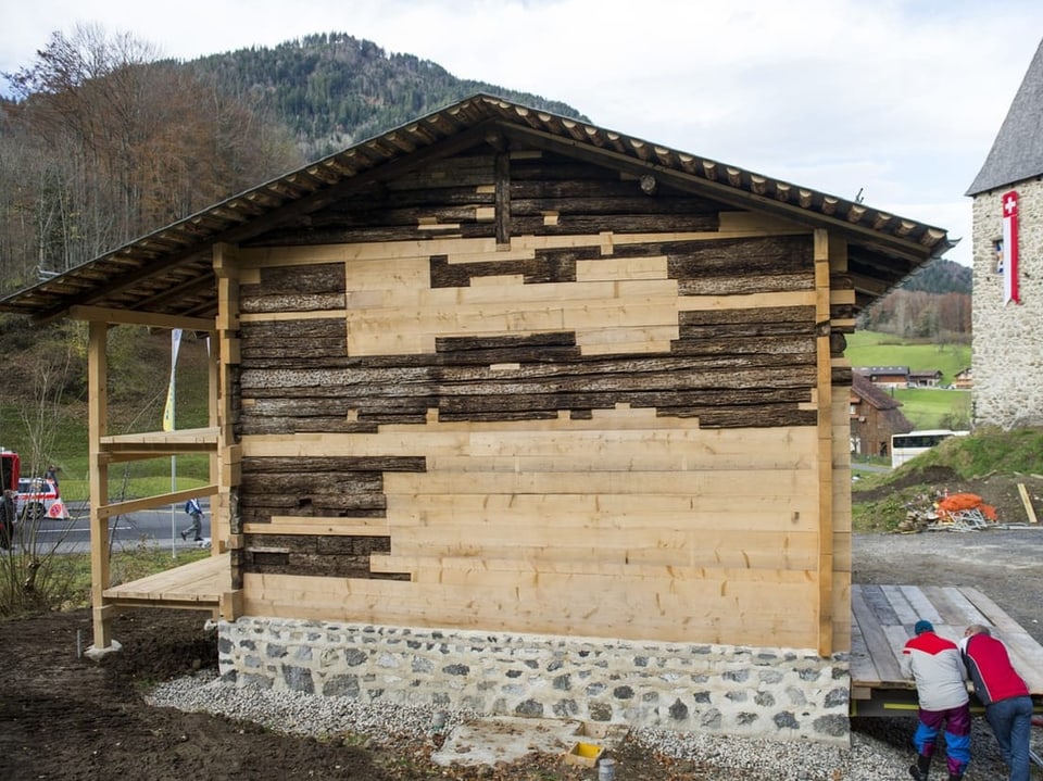 Ein Holzhaus ist zu sehen mit hellen, neuen Brettern sowie alten, dunklen.