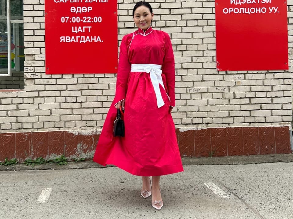 Frau in rotem Kleid vor Ziegelwand mit roten Schildern.