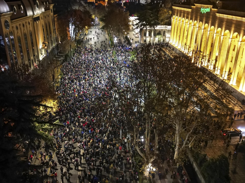 Grosse Menschenmenge versammelt in beleuchteter Stadtstrasse bei Nacht.