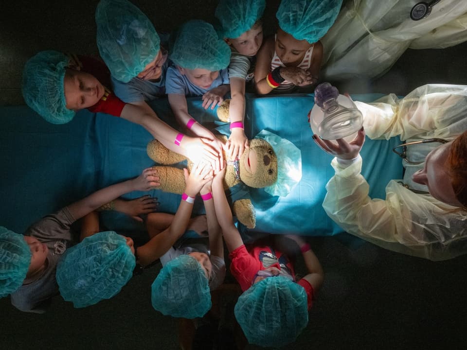 Kinder in OP-Kappen beiwohnen einem Teddybär-Operation mit Arzt.