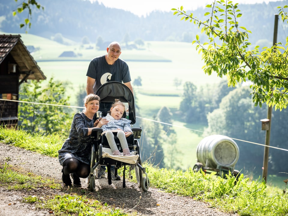 Eine Mutter und ein Vater schieben ein Kind in einem Wagen.