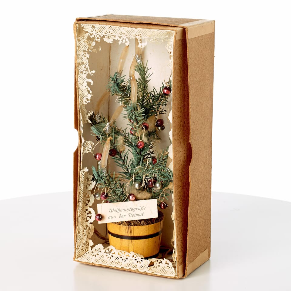 Ein Mini-Weihnachtsbaum in einer kleinen Kartonbox. Auf einer Etikette steht «Weihnachtsgrüsse aus der Heimat».