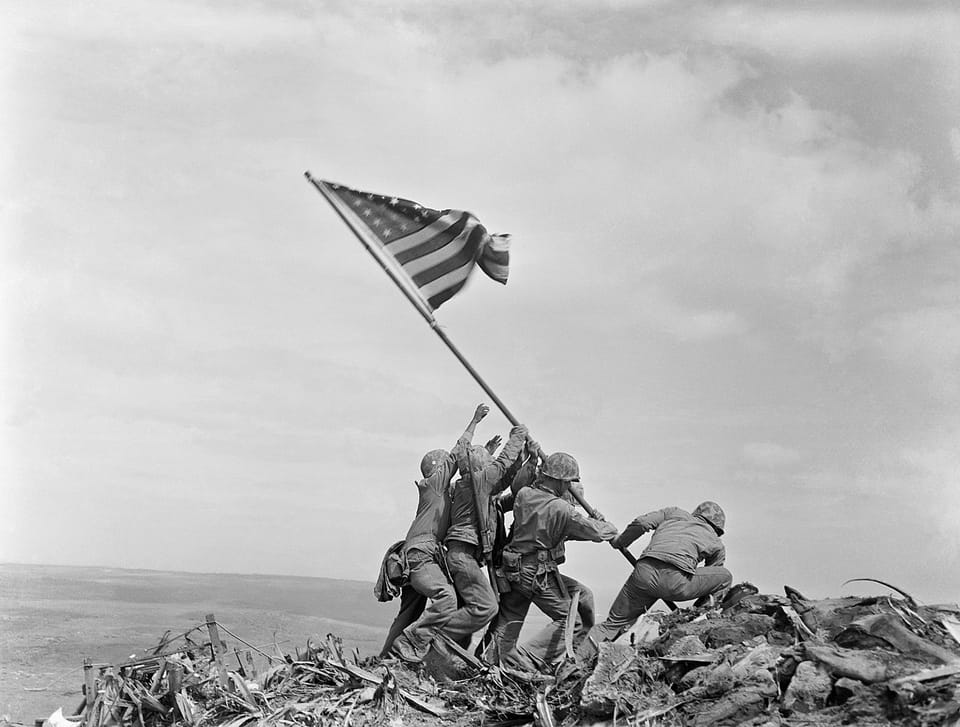Vier Männer hissen auf einem Hügel die amerikanische Flagge