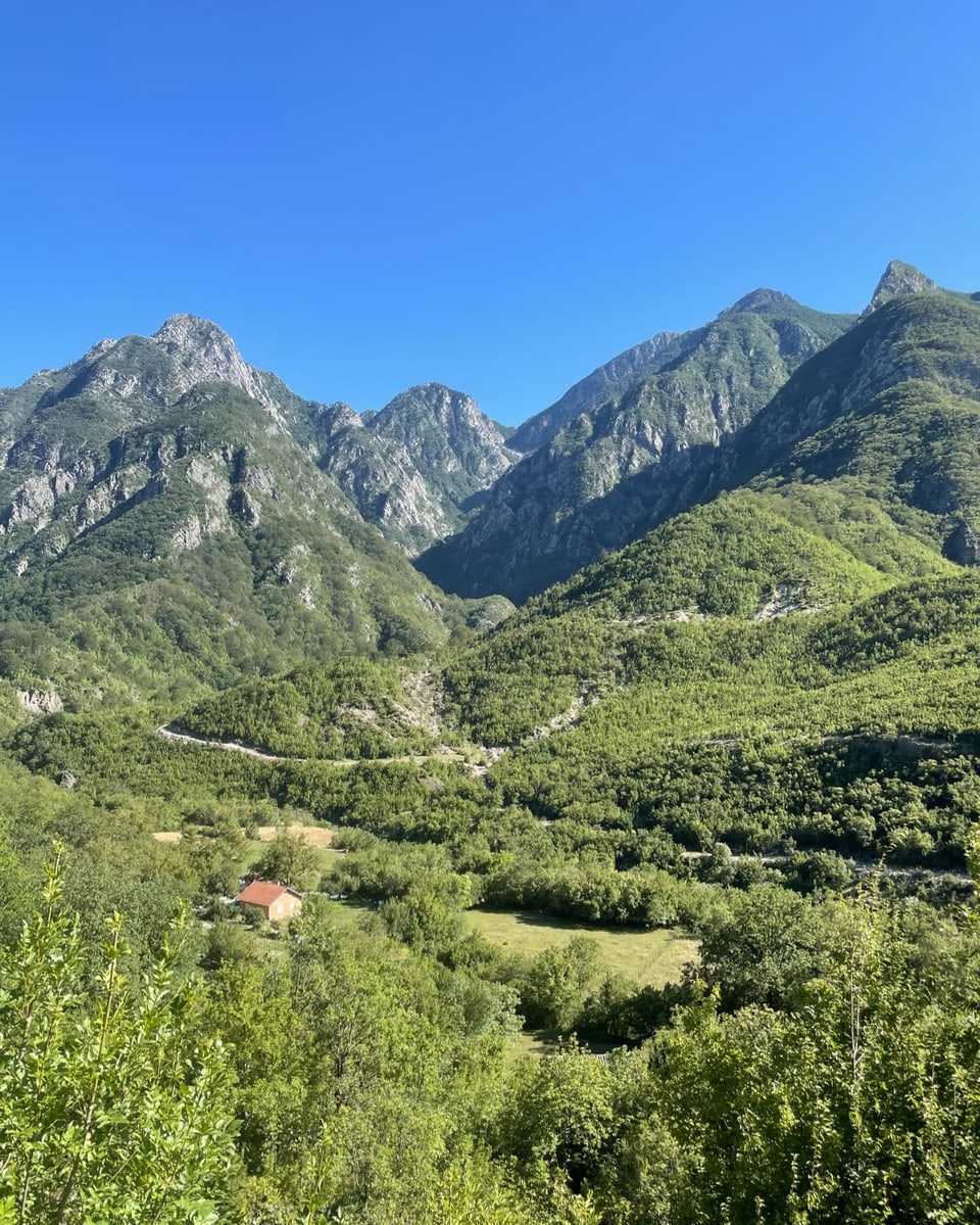 Grüne Berglandschaft unter klarem blauem Himmel.