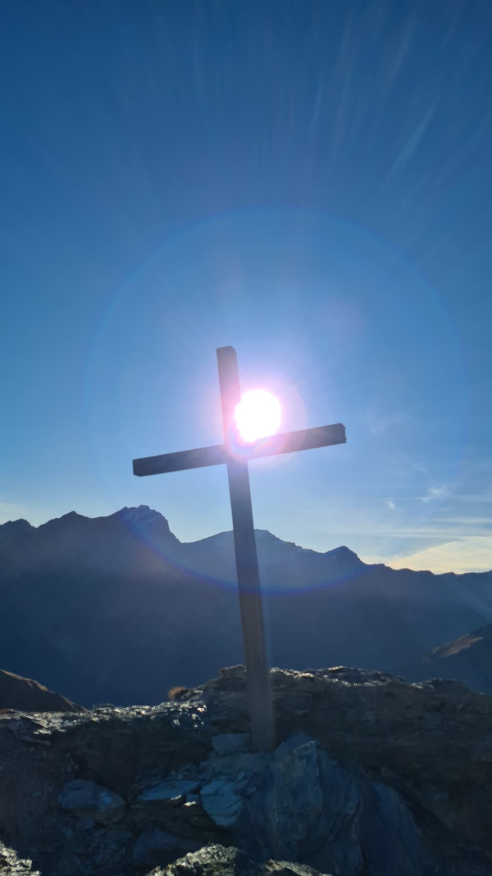 Holzkreuz auf Berggipfel im Sonnenlicht.