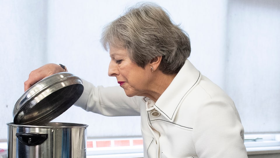 Theresa May schaut in einen Kochtopf.