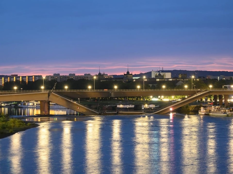 Beleuchtete Brücke bei Sonnenuntergang, reflektierend im Wasser.