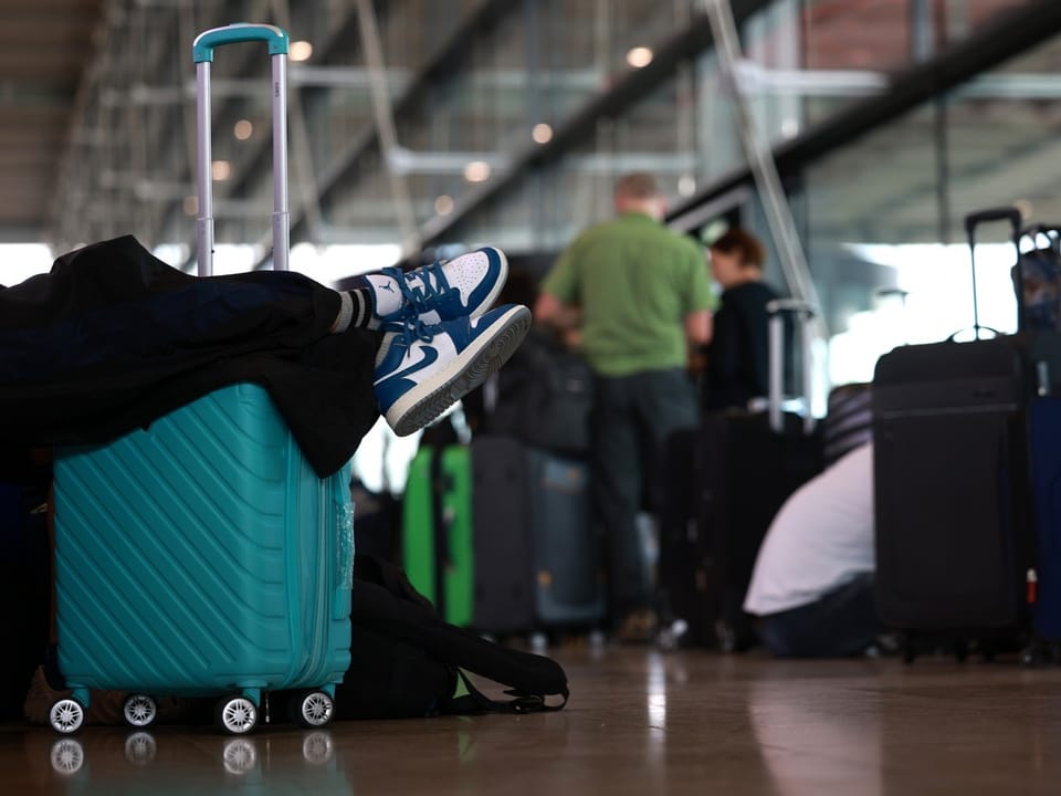 Person im Flughafen mit Beinen auf einem Koffer.