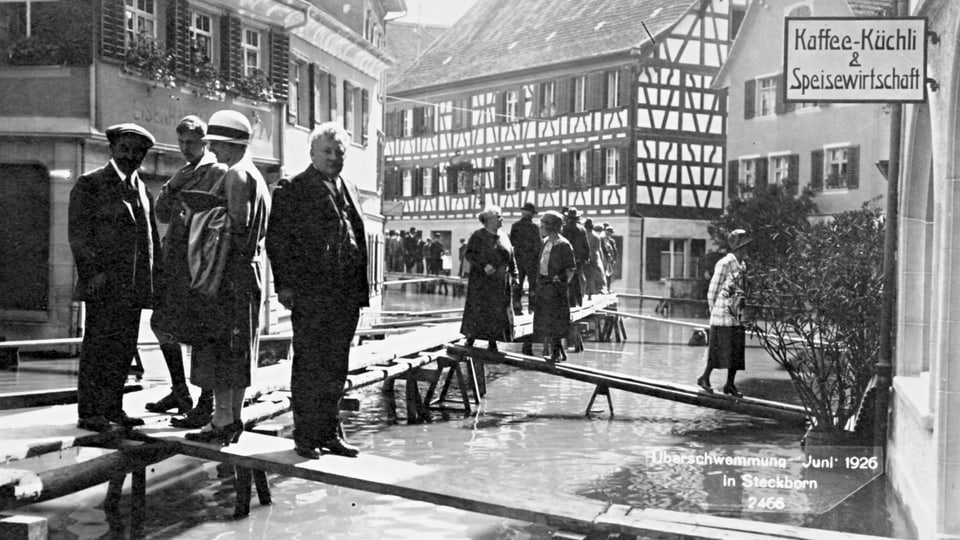 Menschen gehen auf provisorischen Stegen über Hochwasserstrasse, Steckborn, Juni 1926.