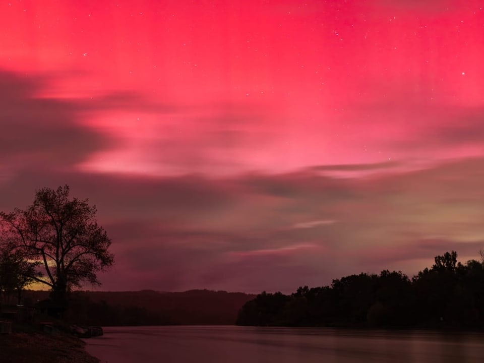 Rote Polarlichter über einem Fluss und Bäumen.