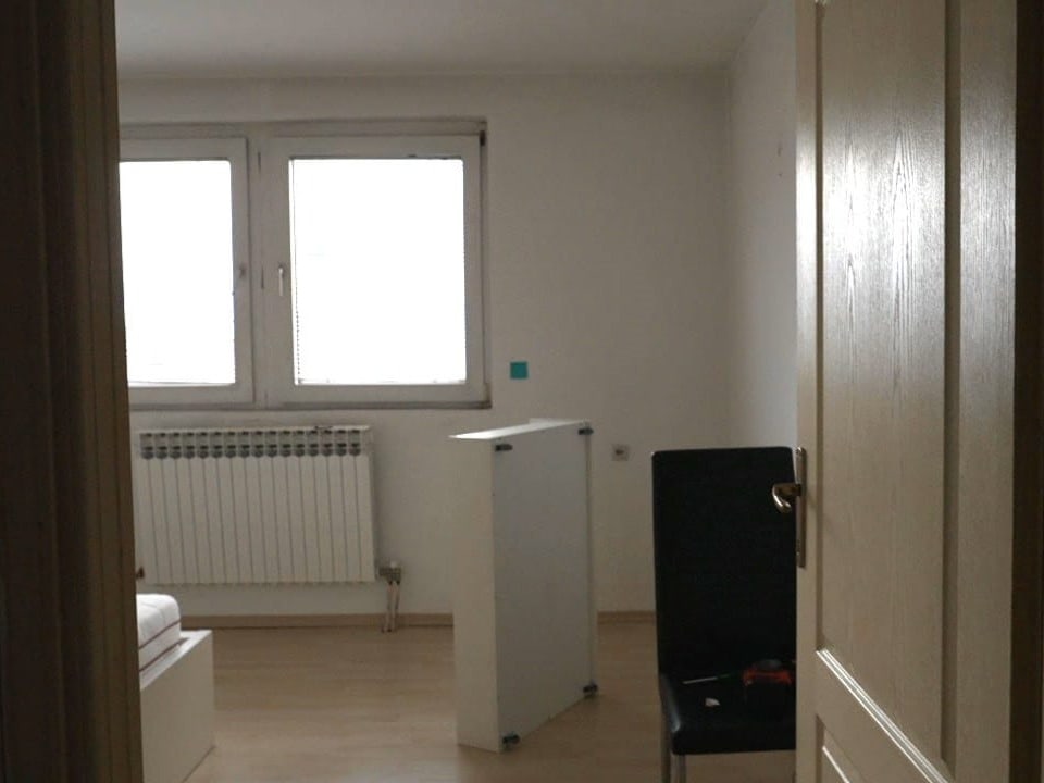 Leeres Zimmer mit zwei Fenstern und einem Heizkörper.