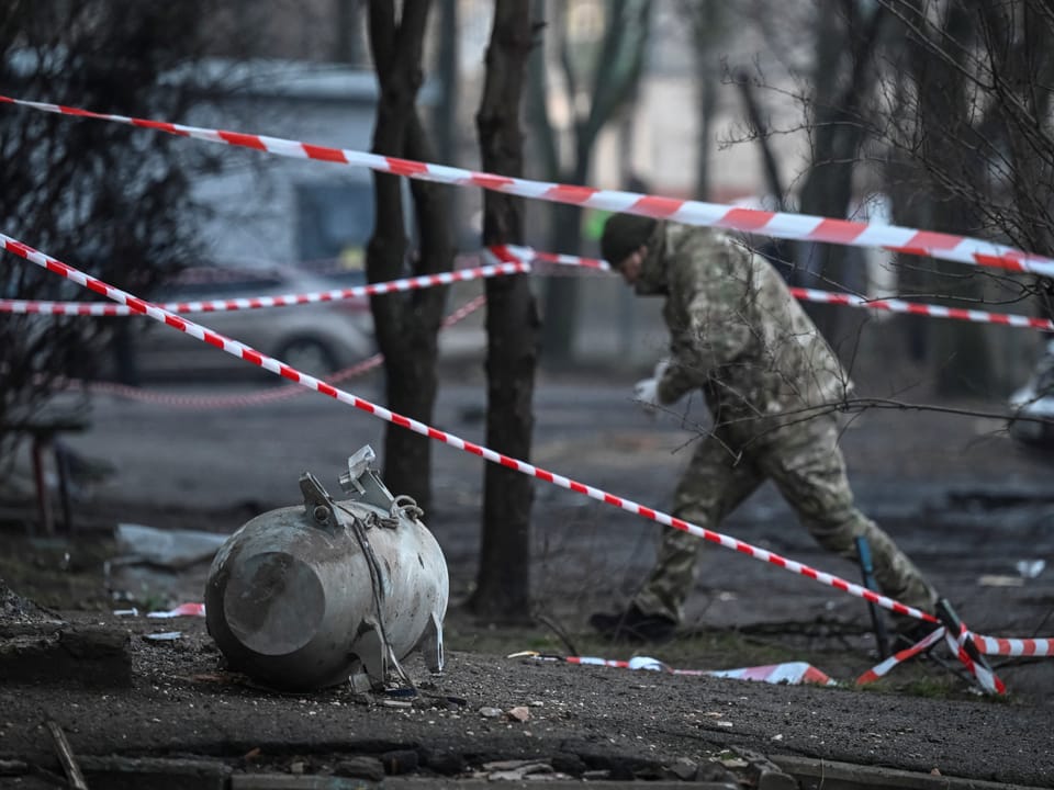 Soldat inspiziert Bombe, Absperrband im Hintergrund.