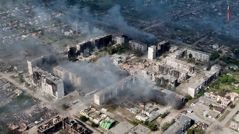 Luftaufnahme einer zerstörten Stadt mit rauchenden Gebäuden.