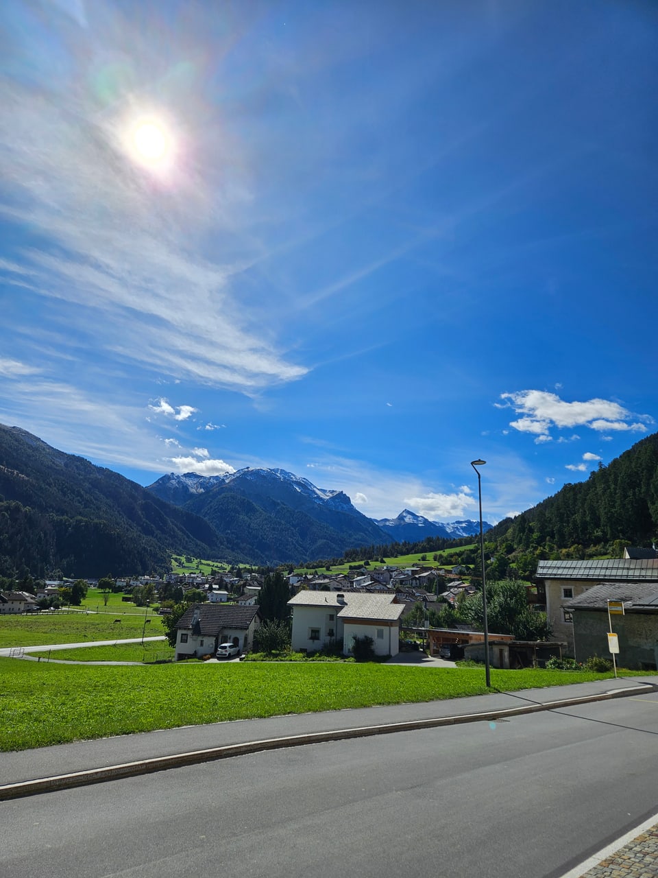 Sonniger Blick auf ein Dorf in den Alpen mit Bergen im Hintergrund.