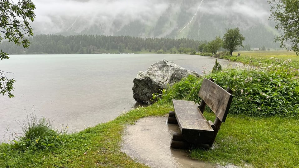 Blick auf den Silsersee und eine Sitzbank mit Pfütze.