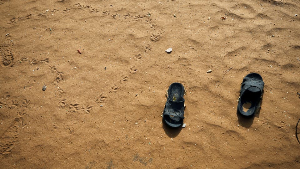 Zwei Sandaletten sind auf einem sandigen Boden zu sehen.