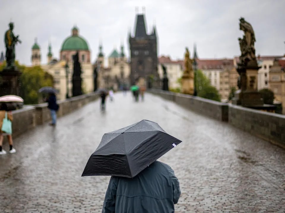 Person mit Regenschirm auf nasser Brücke in Prag.