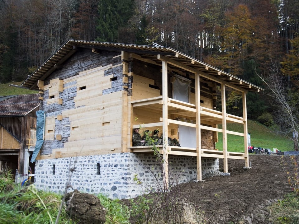 Ein Holzhaus ist zu sehen mit hellen, neuen Brettern sowie alten, dunklen und einer Veranda.