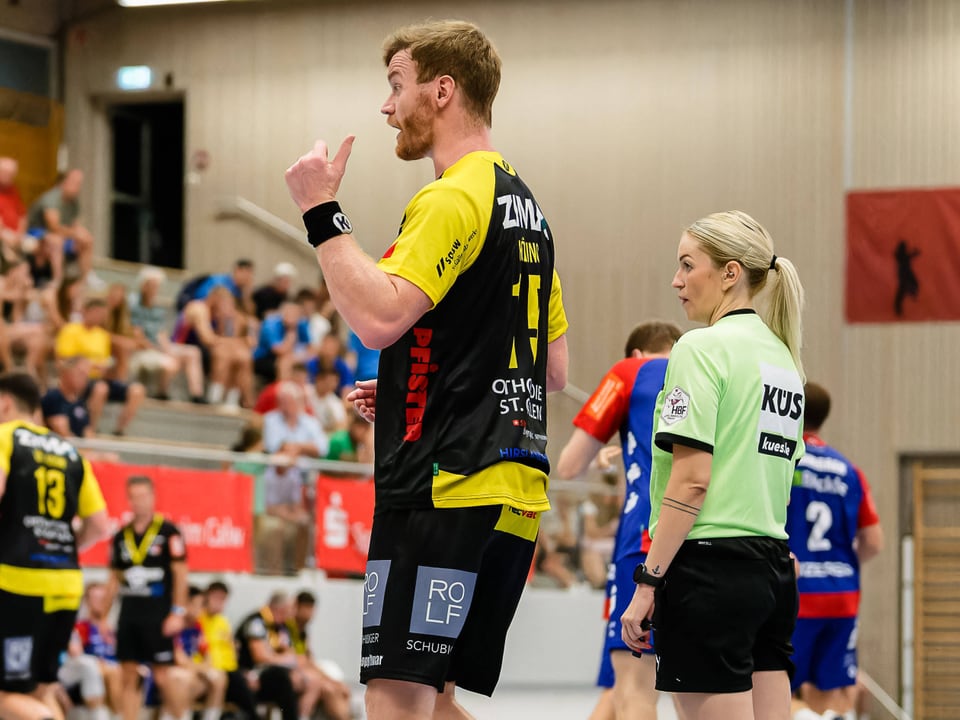 Handballspieler im gelben Trikot mit Schiedsrichterin in Sporthalle.