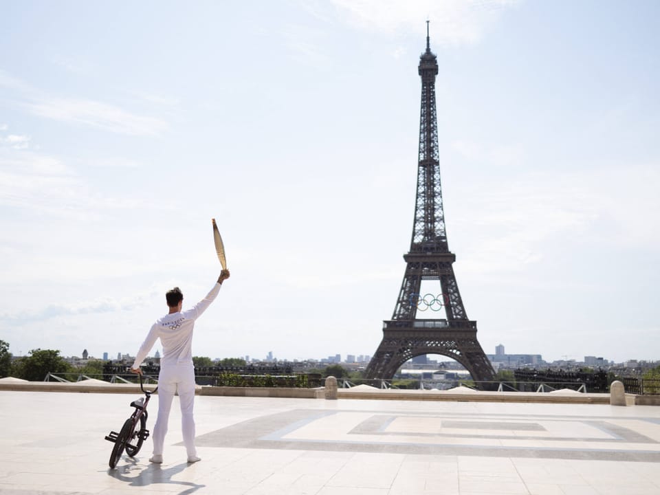 BMX-Fahrer hält die goldene olympische Flamme hoch, mit Blick auf den Eiffelturm