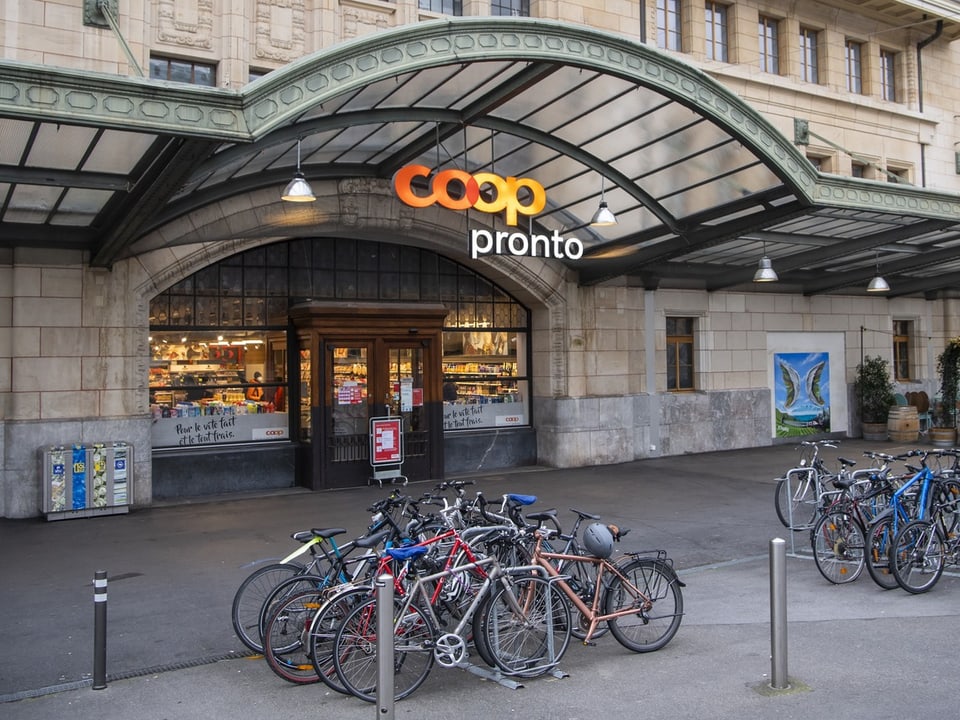 Fahrräder vor Coop Pronto Filiale mit gewölbter Glasüberdachung.