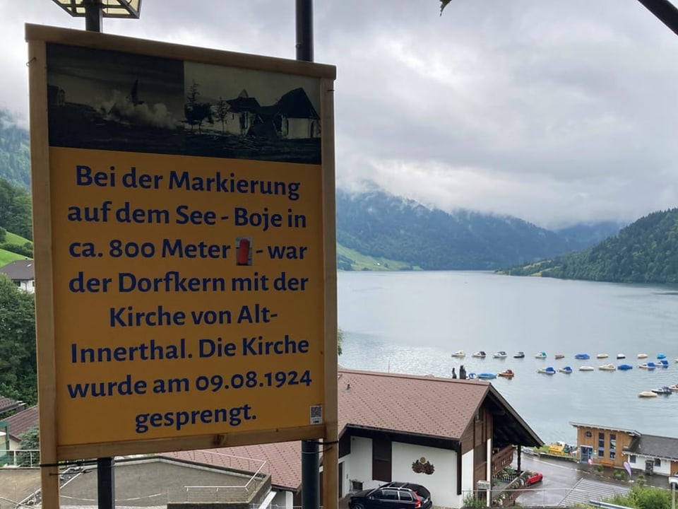 Schild mit Text, dass eine Boje den Dorfkern mit Kirche im See markiert.