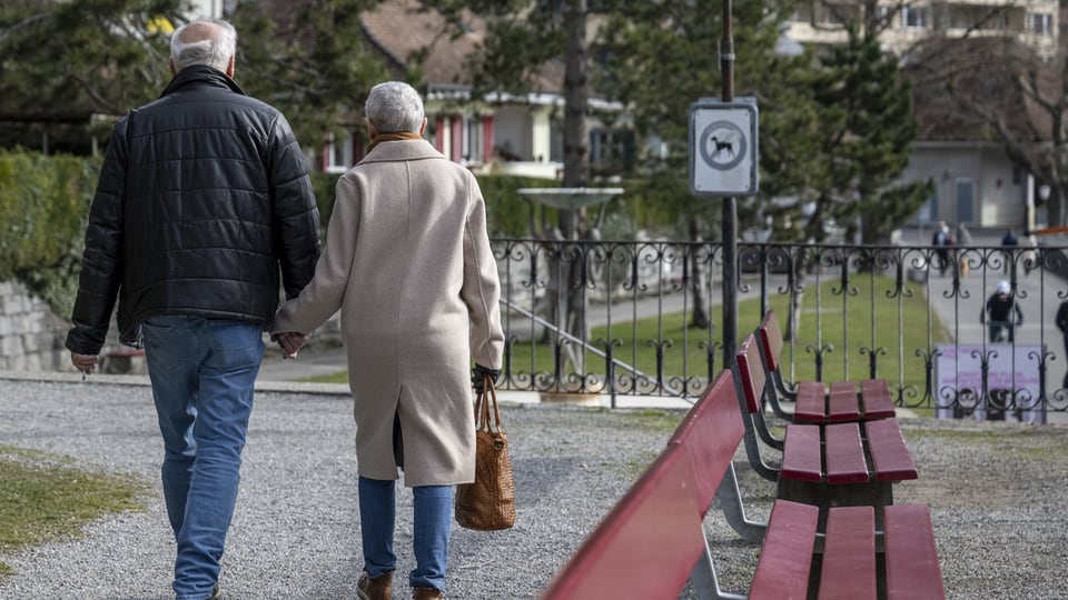 Ein älteres Paar geht Hand in Hand auf einem Kiesweg.