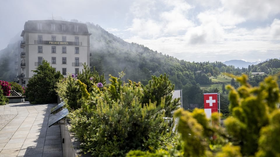 Palasthotel vor bewaldeten Bergen und Schweizer Flagge.