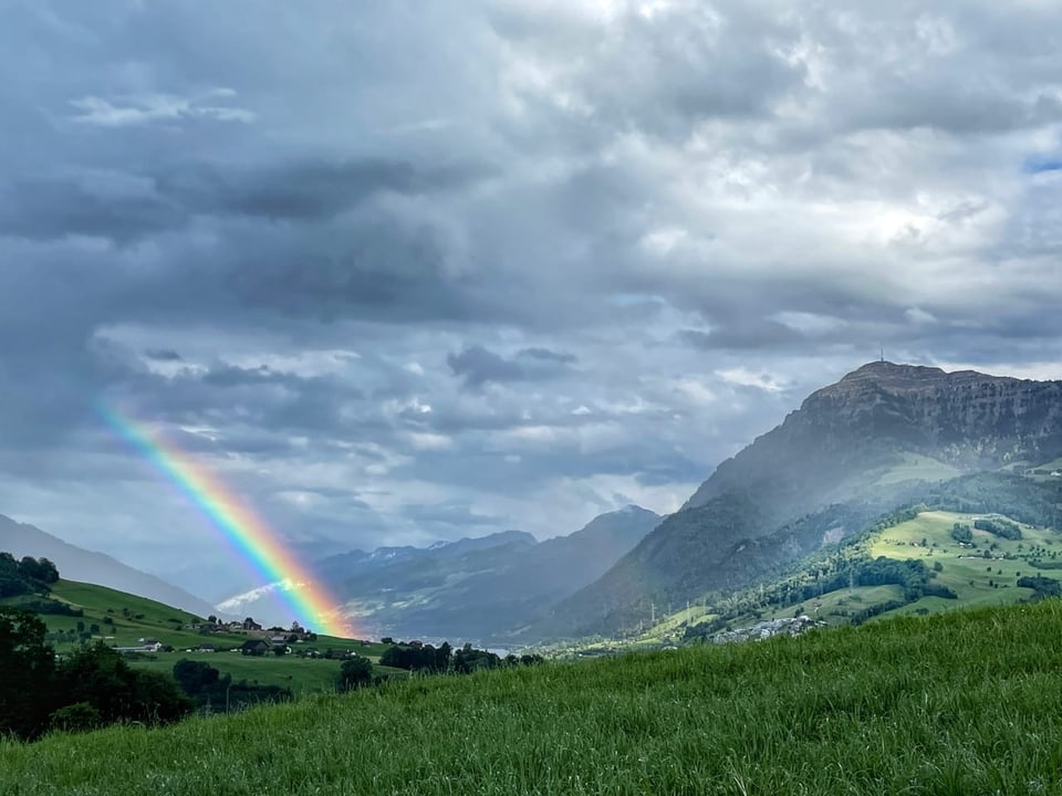 Regenbogen über einem Tal mit Bergen und Wolken.