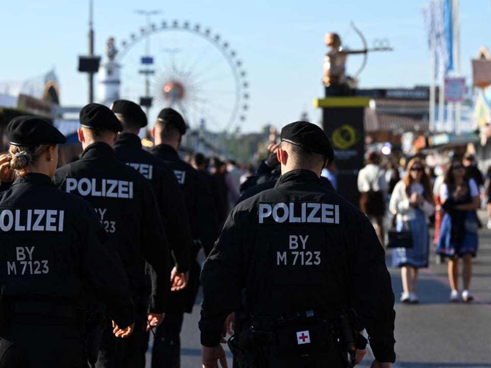 Polizisten in schwarzer Uniform patrouillieren auf einem Volksfest.