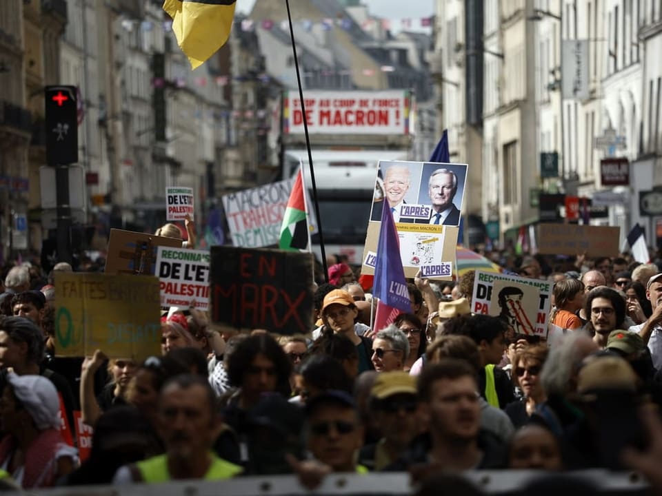 Menschenmenge bei einer Demonstration auf einer Stadtstrasse mit Schildern und Bannern.