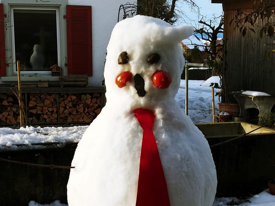 Schneemann mit rotem Schal im Garten.