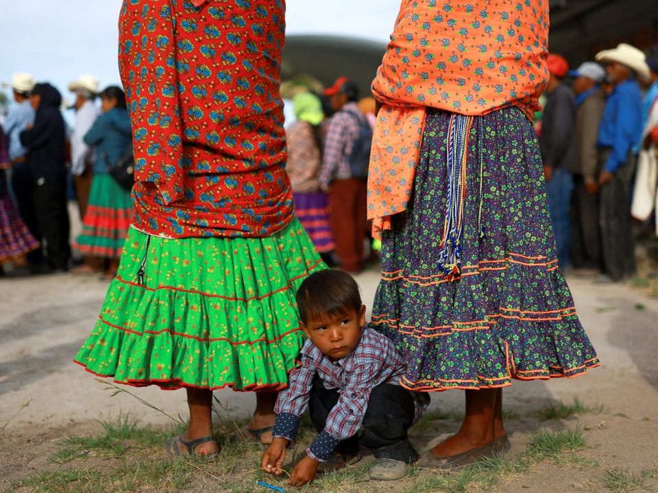 Ein kleiner Junge kauert zwischen zwei in farbigen Röcken und Tüchern gekleideten Frauen