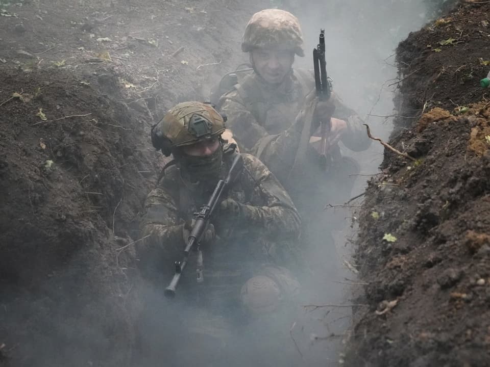 Zwei Soldaten gehen durch einen schmalen, rauchigen Graben.