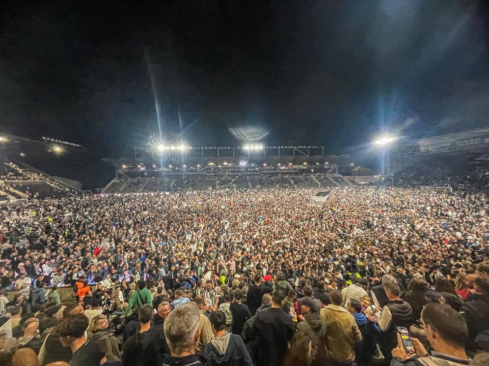 Grosse Menschenmenge bei Nacht in einem beleuchteten Stadion.